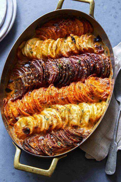 Layered root vegetable tian with sliced carrots, potatoes, and onions in a creamy sauce